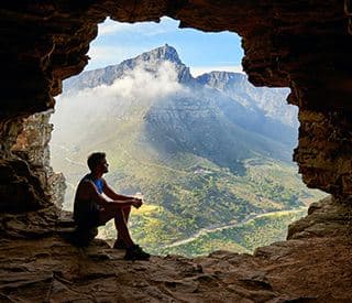 Person sitting in cave with mountain view